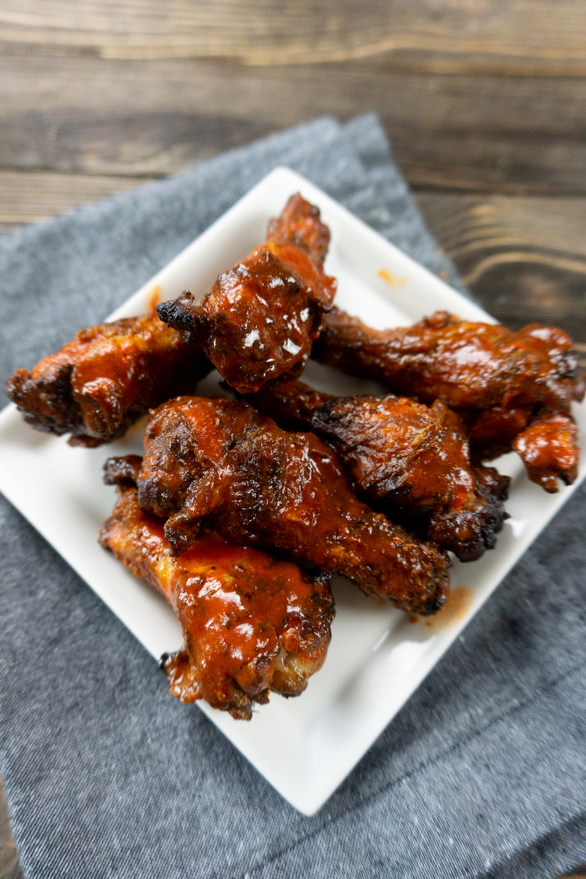 smoked buffalo wings on a square white plate, sitting on a dark wooden table, over a gray hand towel