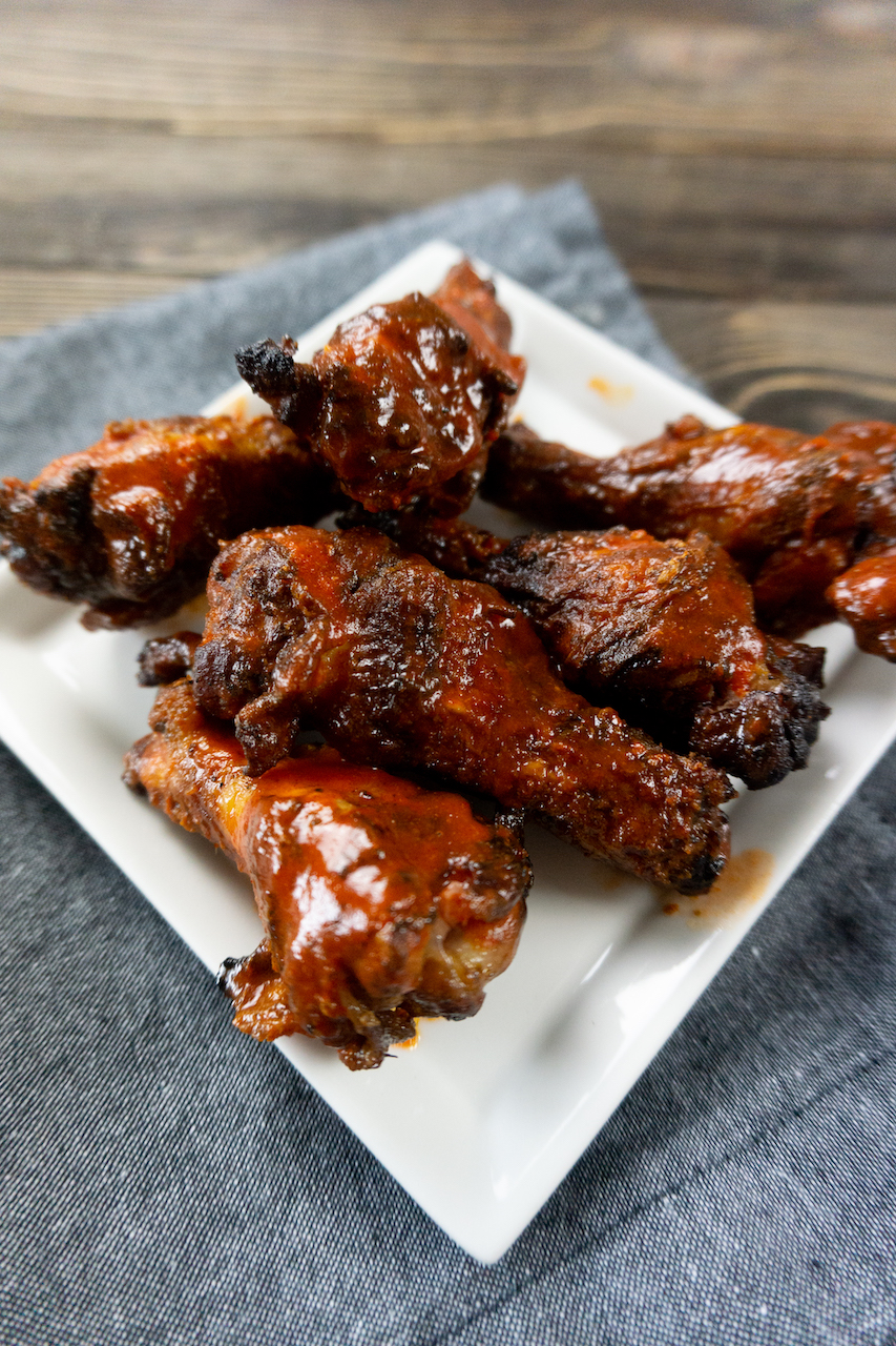 wings on a square white plate sitting on top of a wooden table with a gray towel